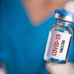 Person holding a vial labeled COVID-19 Vaccine.