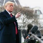 Man speaking to microphones, pointing outdoors.