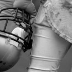 Football player holding helmet, dirty uniform close-up.