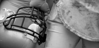 Football player holding helmet, dirty uniform close-up.
