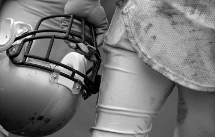 Football player holding helmet, dirty uniform close-up.