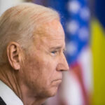 Joe Biden, side profile, flags behind.
