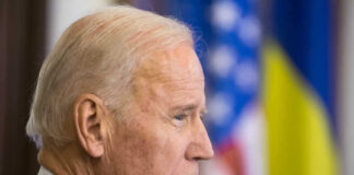 Joe Biden, side profile, flags behind.