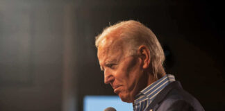 Man holding microphone, wearing suit, looking downward thoughtfully.