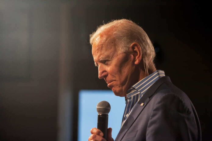 Man holding microphone, wearing suit, looking downward thoughtfully.