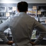 Man examining investigation board with photos and notes.