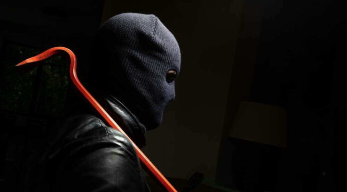 Person in ski mask holding a crowbar