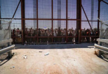 Illegal aliens standing behind a fence