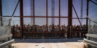 Illegal aliens standing behind a fence