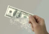 Hand holding a disintegrating hundred dollar bill