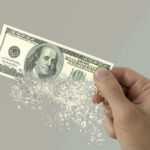 Hand holding a disintegrating hundred dollar bill