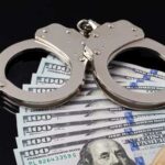 Handcuffs resting on a stack of hundred dollar bills