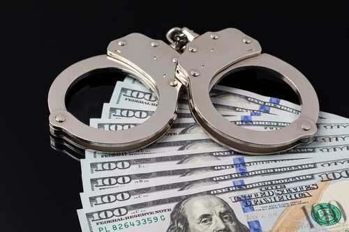 Handcuffs resting on a stack of hundred dollar bills