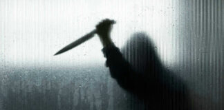 Backlit silhouette holding a knife through frosted glass