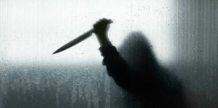 Backlit silhouette holding a knife through frosted glass
