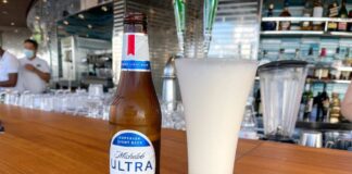 A bottle of Michelob Ultra next to a glass of beer on a wooden bar