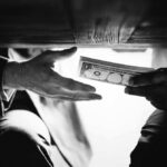 Hands passing money under a table, shrouded in mystery.