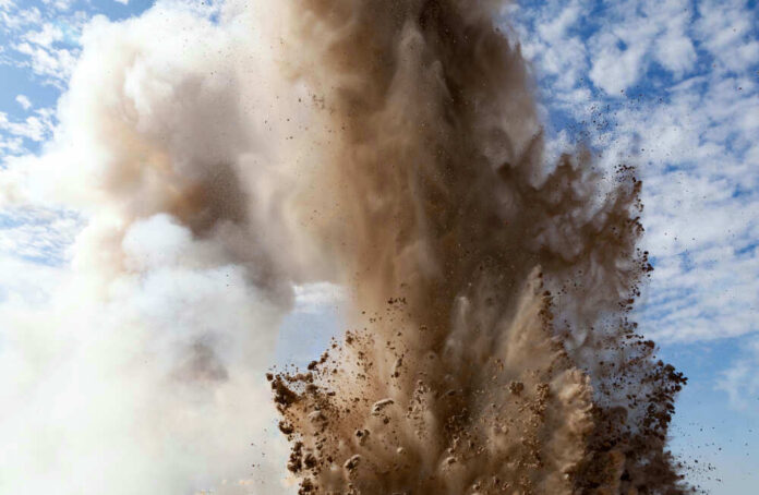 Explosion of dirt and debris against a cloudy sky.