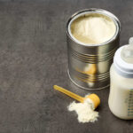 A can of powdered baby formula next to a feeding bottle with milk