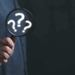 Hand holding magnifying glass with question marks.
