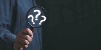 Hand holding magnifying glass with question marks.
