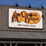 Sign for Cracker Barrel Old Country Store featuring a man sitting on a barrel