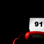 911 Call Turns Deadly In Kitchen A red telephone next to a sign displaying the number 911 on a dark background