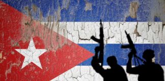 Silhouettes of armed figures in front of a weathered Cuban flag