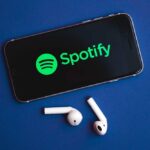 Smartphone displaying the Spotify logo with wireless earbuds nearby