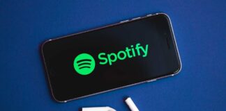 Smartphone displaying the Spotify logo with wireless earbuds nearby