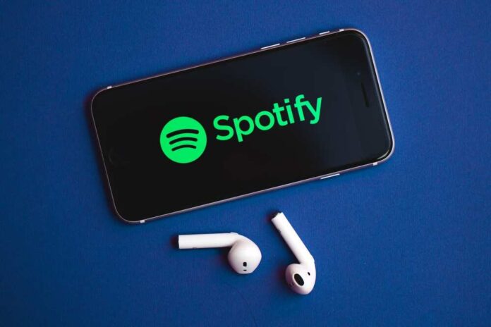 Smartphone displaying the Spotify logo with wireless earbuds nearby