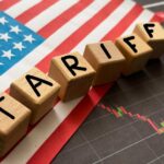 Wooden blocks spelling 'TARIFFS' on a background of the US flag and financial charts