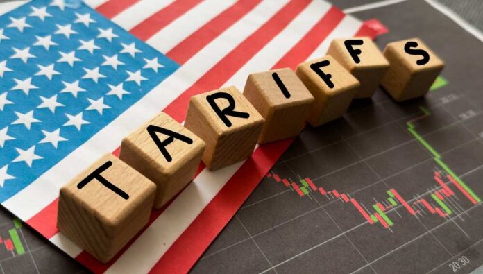 Wooden blocks spelling 'TARIFFS' on a background of the US flag and financial charts