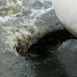 Industrial pipe discharging dark water into a body of water