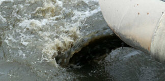 Industrial pipe discharging dark water into a body of water