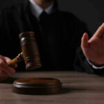 Judge holding gavel, hand raised in courtroom.