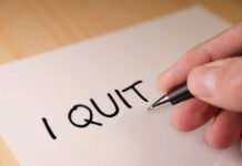 A hand writing 'I QUIT' on a piece of paper