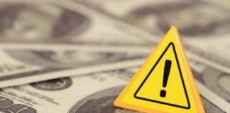 A yellow warning sign on a background of dollar bills