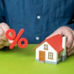 Person holding a percentage symbol above a model house