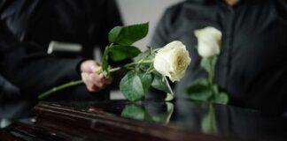 Two individuals placing white roses on a coffin during a funeral