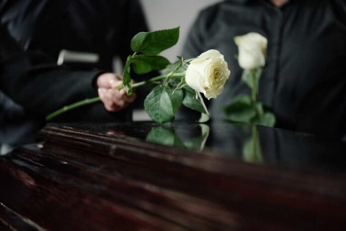 shutterstock_2684119419.jpg Two individuals placing white roses on a coffin during a funeral