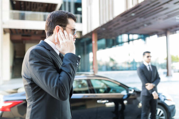 Security personnel in a suit communicating via earpiece near a car