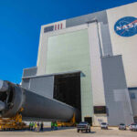 Massive rocket component outside NASA assembly building under clear sky.
