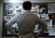 Man examining investigation board with photos and notes.