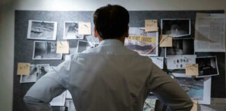 Man examining investigation board with photos and notes.