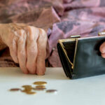 Elderly hands with purse and coins on table.