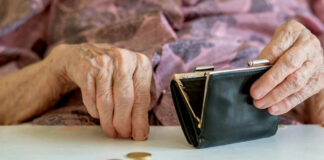 Elderly hands with purse and coins on table.