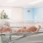Newborn baby lying in a transparent crib in a hospital nursery