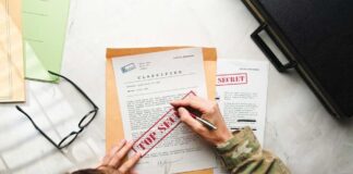 A person in military attire marking a classified document with a red 'FOR SECRET' stamp