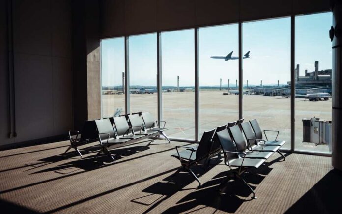 shutterstock_2473276511.jpg View of an airport waiting area with an airplane taking off in the background
